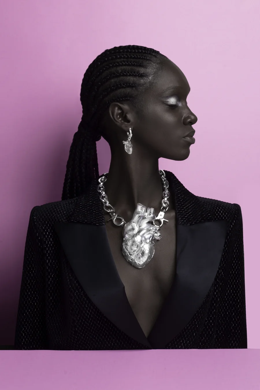 Daha Garcés de perfil, con blazer negro y un collar de plata en forma de corazón, sobre fondo lila