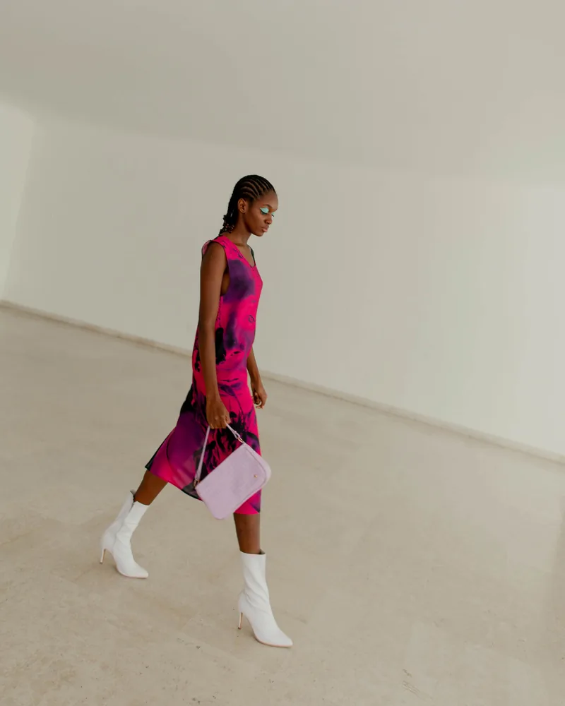 Modelo caminando con vestido estampado y botas blancas en un estudio claro